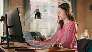 Young Pretty Female in Pink Jumper Working from Home on Desktop Computer. Creative Woman Checking