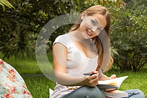 Young pretty female student with books working in a park