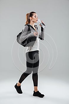 Young pretty fitness woman carrying sports bag and drinking water