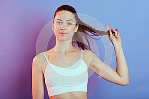 Young pretty fitness woman pulling her ponytail aside posing isolated over color background, looking directly at camera, wearing