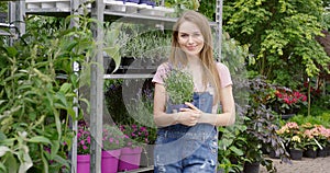 Young pretty gardener woman posing at stand with potted flowers