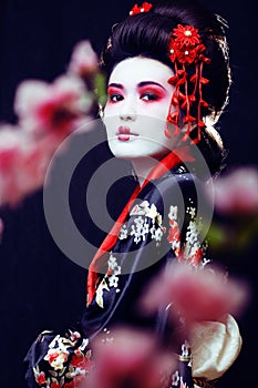 young pretty geisha in kimono with sakura and decoration on blac