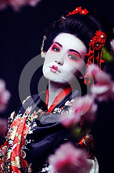 young pretty geisha in kimono with sakura and decoration on blac