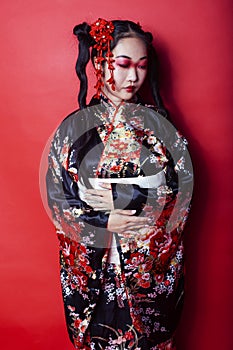 Young pretty geisha on red background posing in kimono, oriental concept