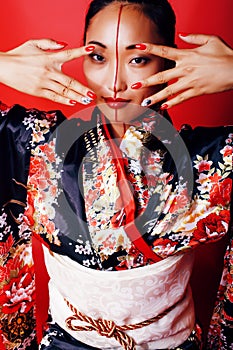 Young pretty geisha on red background posing in kimono, oriental people concept close up