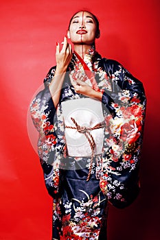 Young pretty geisha on red background posing in kimono, oriental people concept close up