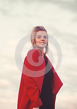 A young pretty girl in an autumn coat laughing and looking at the camera against a blue sky.