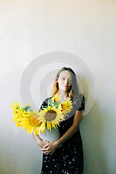 A young pretty girl in a black floral dress holds a vase of sunflower flowers on a white background