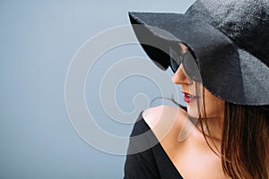 Young pretty girl in a black hat poses against the background of the wall