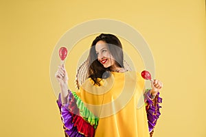 Young pretty girl in bright garment and sombrero isolated over yellow background