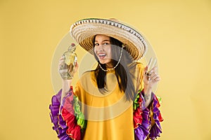 Young pretty girl in bright garment and sombrero isolated over yellow background