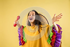 Young pretty girl in bright garment and sombrero  over yellow background