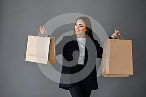 Young pretty girl in business style clothes stands on gray background with paper bags in hands. Business style
