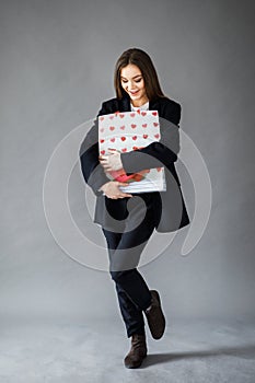 Young pretty girl in business style clothes stands on gray background with paper bags in hands. Business style