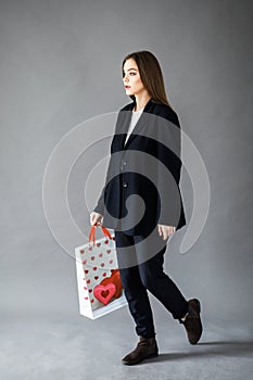 Young pretty girl in business style clothes stands on gray background with paper bags in hands. Business style