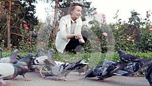 Young pretty girl feeds pigeons in park. Flock of birds eating a loaf bread