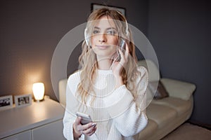 Young pretty girl in headphones with the phone. Listening to music, dancing and singing, indoors