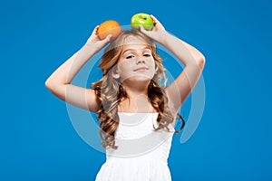Young pretty girl holding apple and orange over blue background.