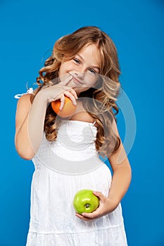 Young pretty girl holding apple and orange over blue background.