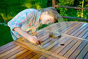 Young pretty girl holding a brush applying varnish paint on a wooden garden table