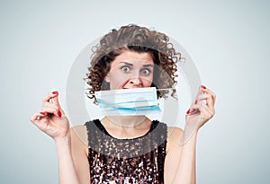 Young pretty girl holding medical respiratory mask with fear expression, on background.