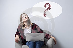 Young girl with a laptop sitting on a soft comfortable chair and thinking, a woman using a computer against a white blank wall,