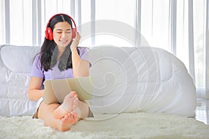Young pretty girl listening to music from home on her bed using computer laptop to access media online