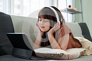 Young pretty girl is lying on a sofa and enjoying listening to music on her headphones