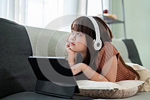 Young pretty girl is lying on a sofa and enjoying listening to music on her headphones