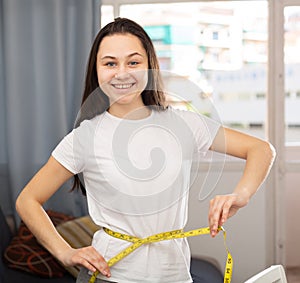 Young pretty girl measuring her waist with measuring tape