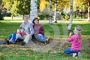 Young pretty girl photographing her family by phone in autumn park