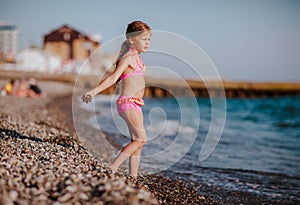 Young pretty girl in pink swim suit having fun at stone sea coast