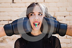 Young and pretty girl with a punkish tendency. She is being hit on each side of her face with boxing gloves while holding a jelly