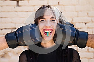 Young and pretty girl with a punkish tendency. She is being hit on each side of her face with boxing gloves while holding a jelly