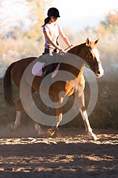 Young pretty girl - riding a horse with backlit leaves behind