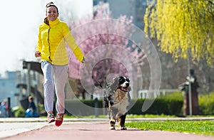 Young pretty girl running outdoor with her Bernese Mountain dog