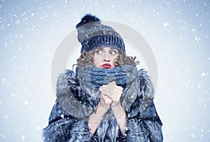 Young pretty girl in a silver fox fur coat, a hat and a scarf warms her hands, there is snow and cold around