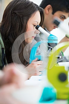 Young pretty girl student peering through microscope