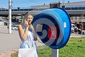 Young pretty girl talking on a payphone on a city street