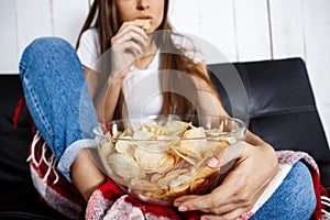 Young pretty girl watching tv, sitting on sofa at home.