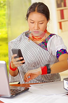 Young pretty girl wearing traditional andean clothing and glasses, sitting working by office desk with laptop computer