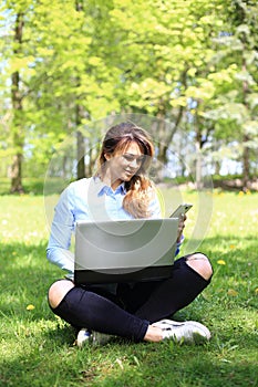 Young pretty girl working on laptop outdoor, lying on grass, caucasian 20 years old