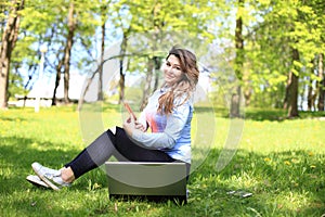 Young pretty girl working on laptop outdoor, lying on grass, caucasian 21 years old