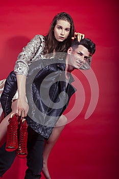 Young pretty guy and girl closed in fashion style after party shoes in hand posing on red background, lifestyle people