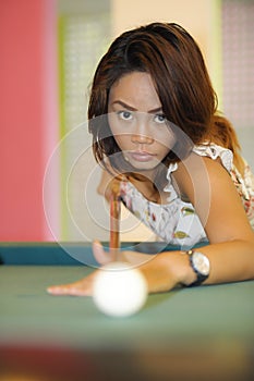 young pretty and happy Asian girl playing snooker holding stick at pool table in night club or bar