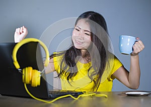 Young pretty and happy Asian Korean woman at desk enjoying internet on laptop computer smiling cheerful having fun drinking tea cu