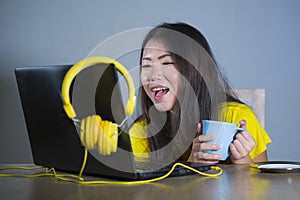 Young pretty and happy Asian Korean woman at desk enjoying internet on laptop computer smiling cheerful having fun drinking tea cu