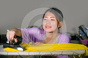 Young pretty and happy Asian Korean woman using iron at home kitchen ironing clothes smiling cheerful and carefree enjoying domest