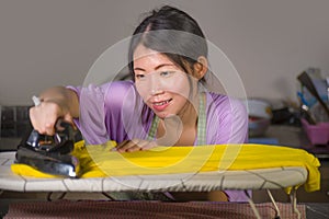 Young pretty and happy Asian Korean woman using iron at home kitchen ironing clothes smiling cheerful and carefree enjoying domest