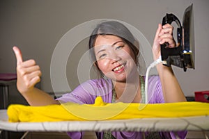 Young pretty and happy Asian Korean woman using iron at home kitchen ironing clothes smiling cheerful and carefree enjoying domest